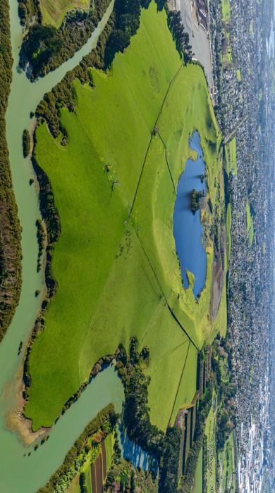 An aerial photo of a volcano surrounded by estuary and urban development, with a lake in the flat centre of the crater.