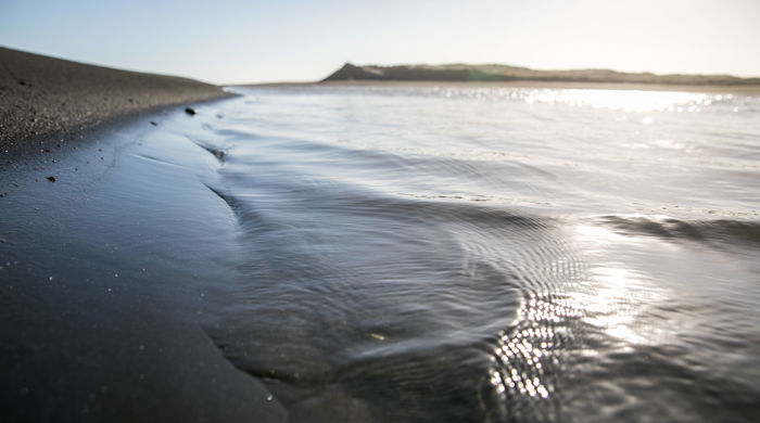 A close-up of the sea water lapping the shore at Raglan. The water is calm with the sun catching the ripples created as it reaches the shore.