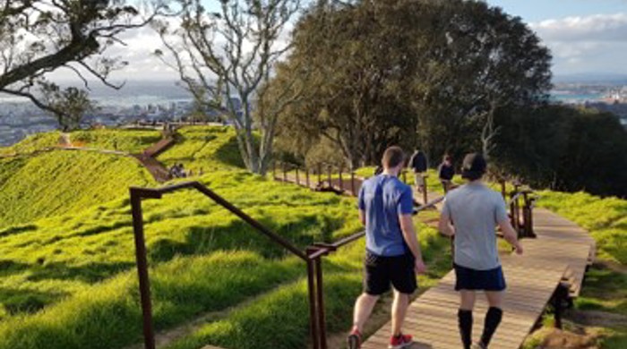 Two people are walking down the boardwalk with a view out over Auckland City in the distance.